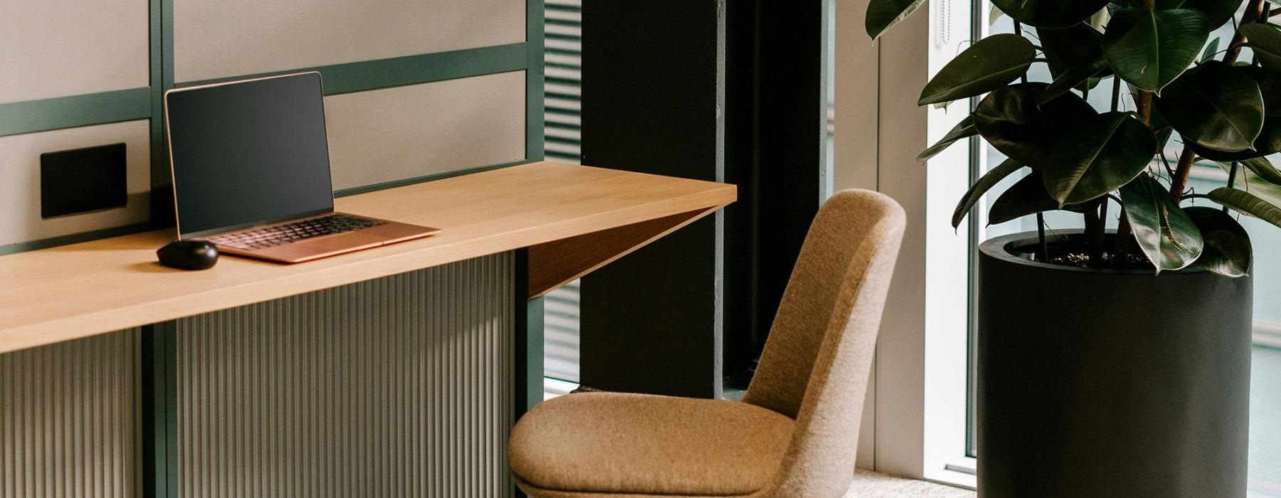 a desk with a laptop and chair near a window and plant