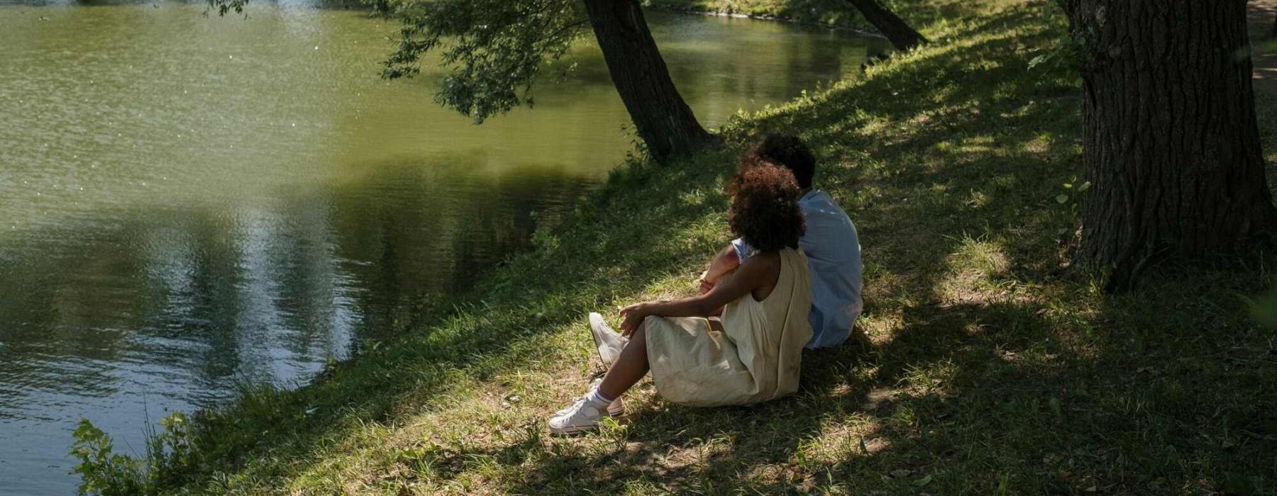a man and woman sitting on a river bank